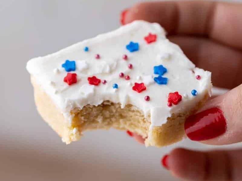 Hand holding a frosted patriotic sugar cookie bar with festive sprinkles