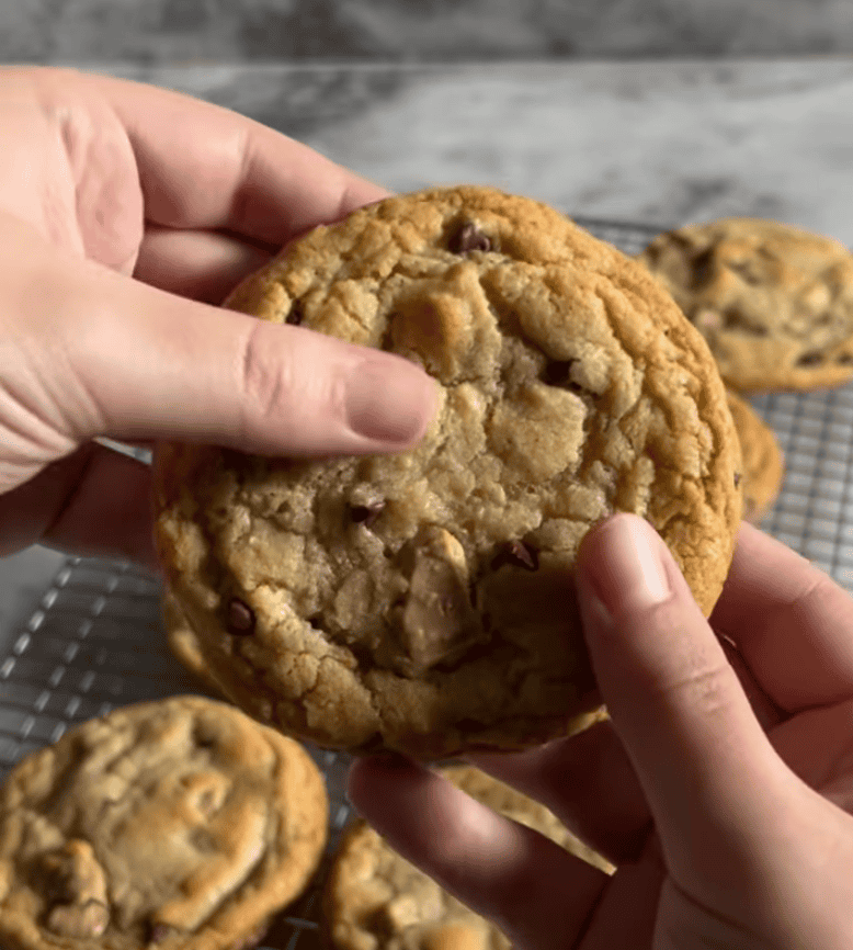 Close-up of a chocolate chip cookie being held over a cooling rack, a community bake from Loaf BakeClub