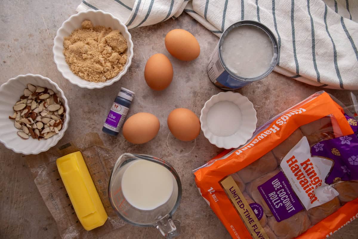 Ingredients for ube French toast bake including King's Hawaiian Ube Coconut rolls, eggs, coconut milk, brown sugar, butter, ube extract, and sliced almonds