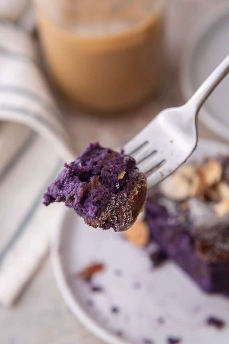 Close up of a forkful of soft purple ube French toast bake with coffee in the background