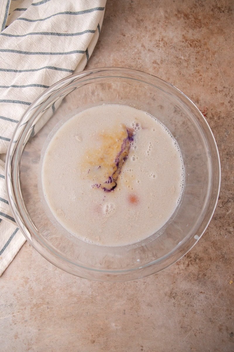 Coconut milk custard with eggs, brown sugar, and ube extract in a glass bowl before whisking
