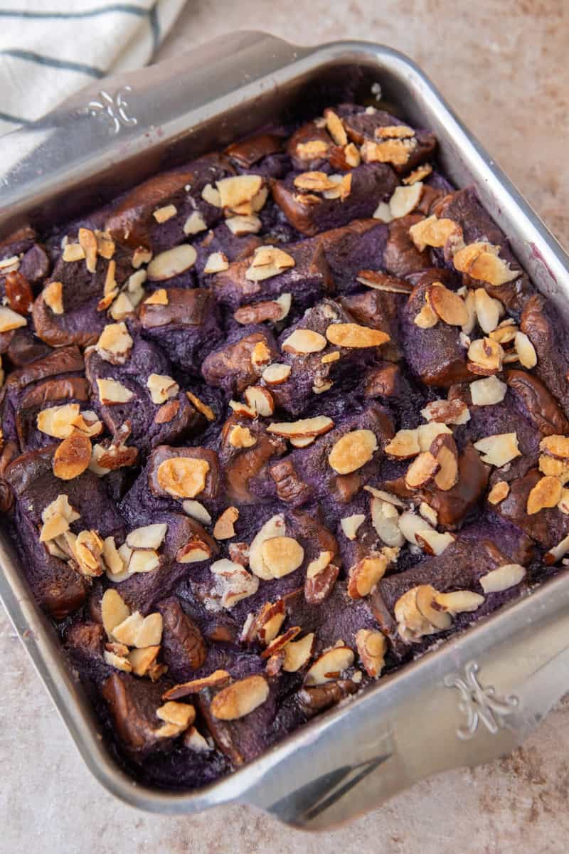 Freshly baked ube French toast bake in a square pan with golden toasted almonds on top