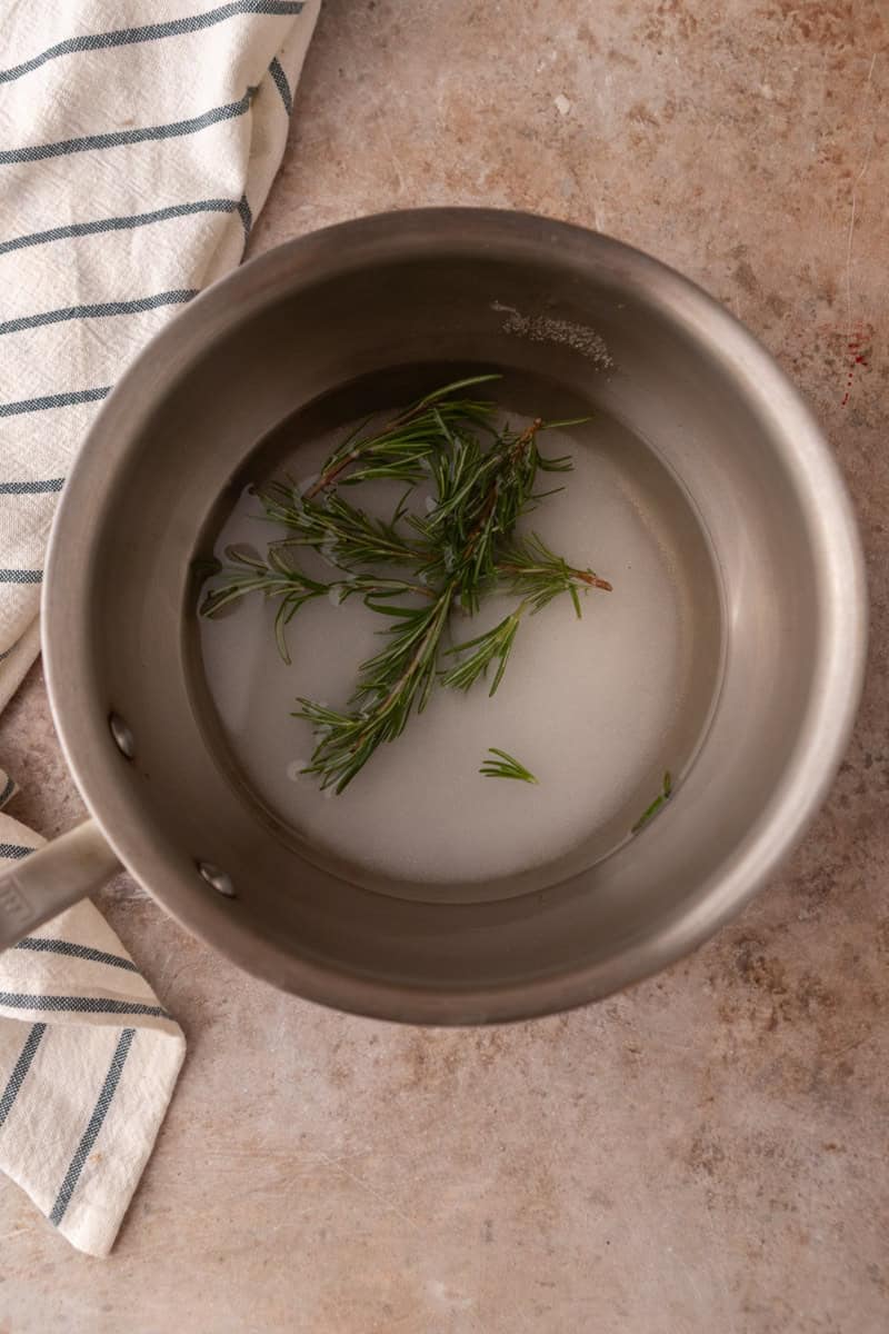 Fresh rosemary sprigs steeping in sugar and water in a saucepan before simmering
