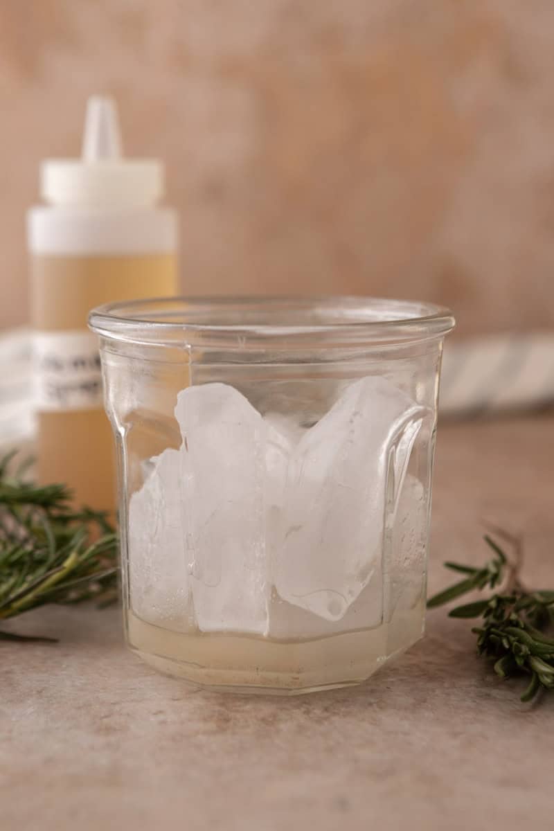 Glass filled with ice and a layer of rosemary vanilla syrup at the bottom