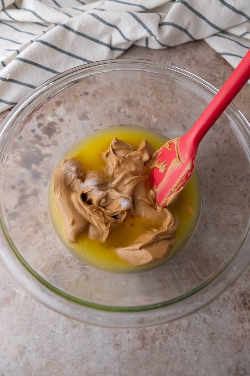 Melted butter and creamy peanut butter in a glass bowl with a red spatula