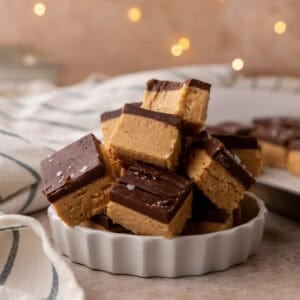 Buckeye fudge squares stacked in a white fluted dish and topped with flaky salt.