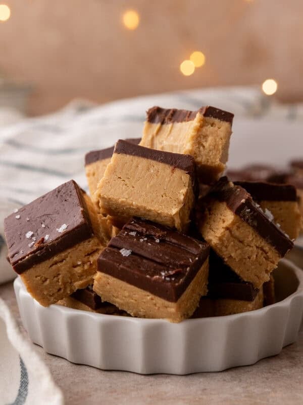 Buckeye fudge squares stacked in a white fluted dish and topped with flaky salt.