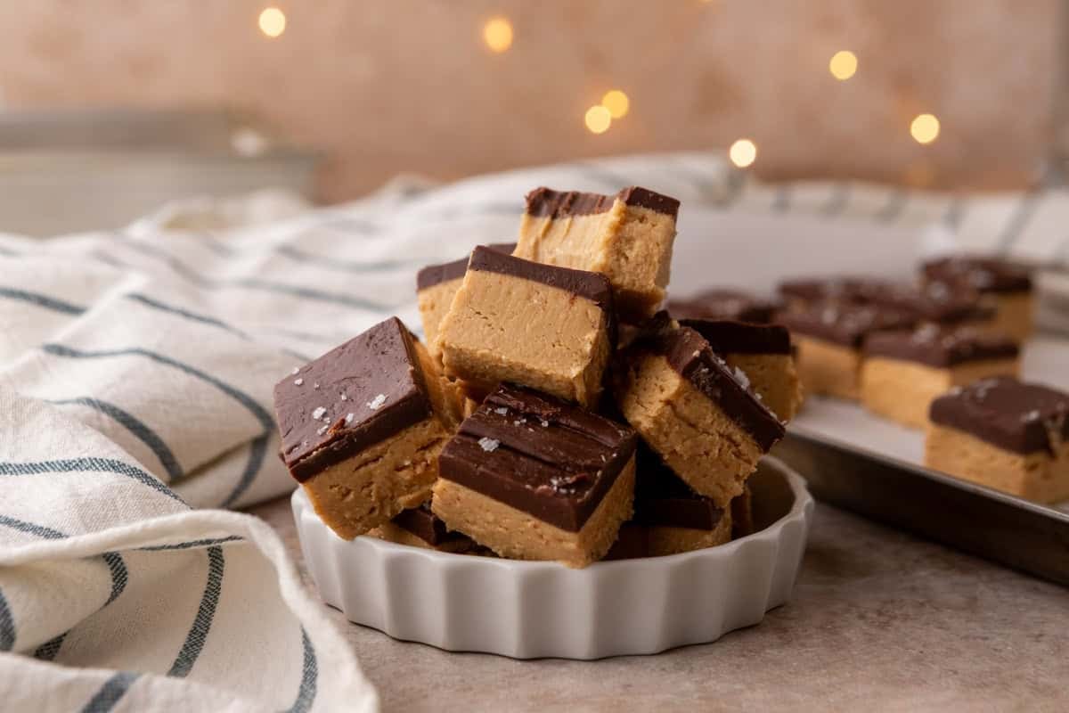 Buckeye fudge squares stacked in a white fluted dish topped with flaky salt