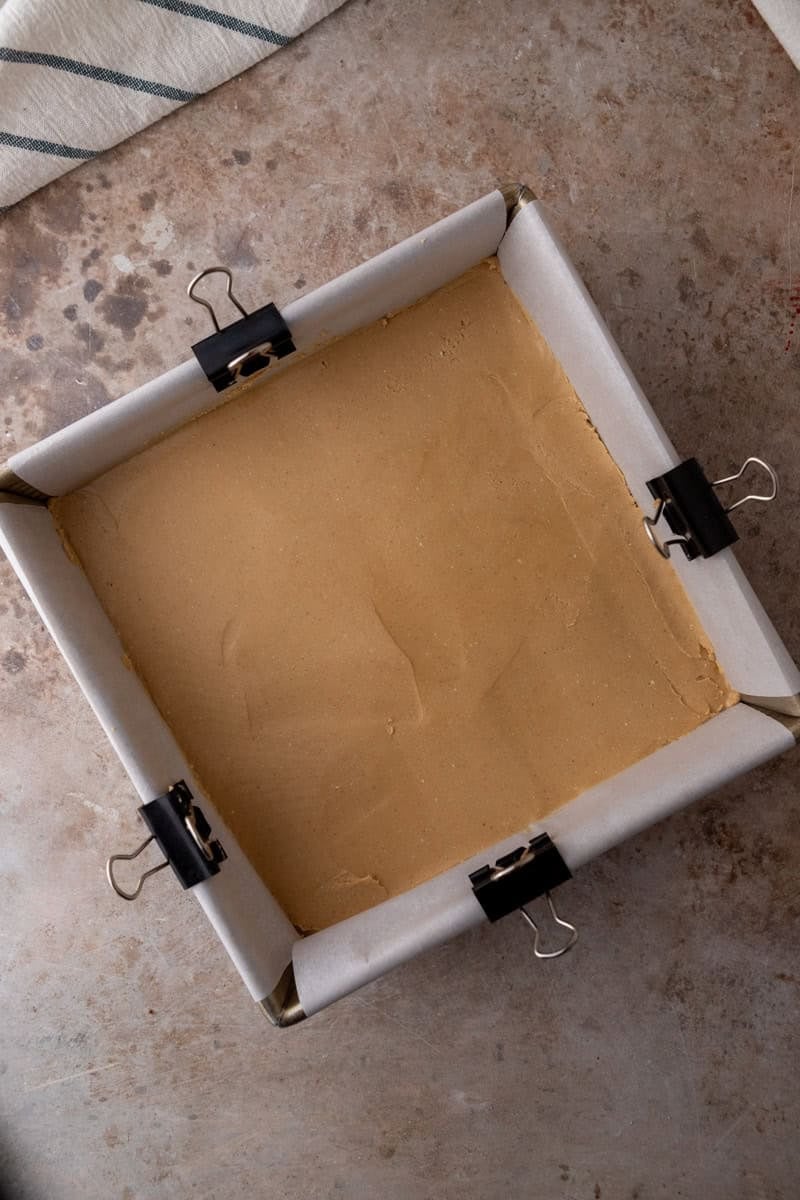 Peanut butter buckeye fudge layer pressed into a parchment lined square pan