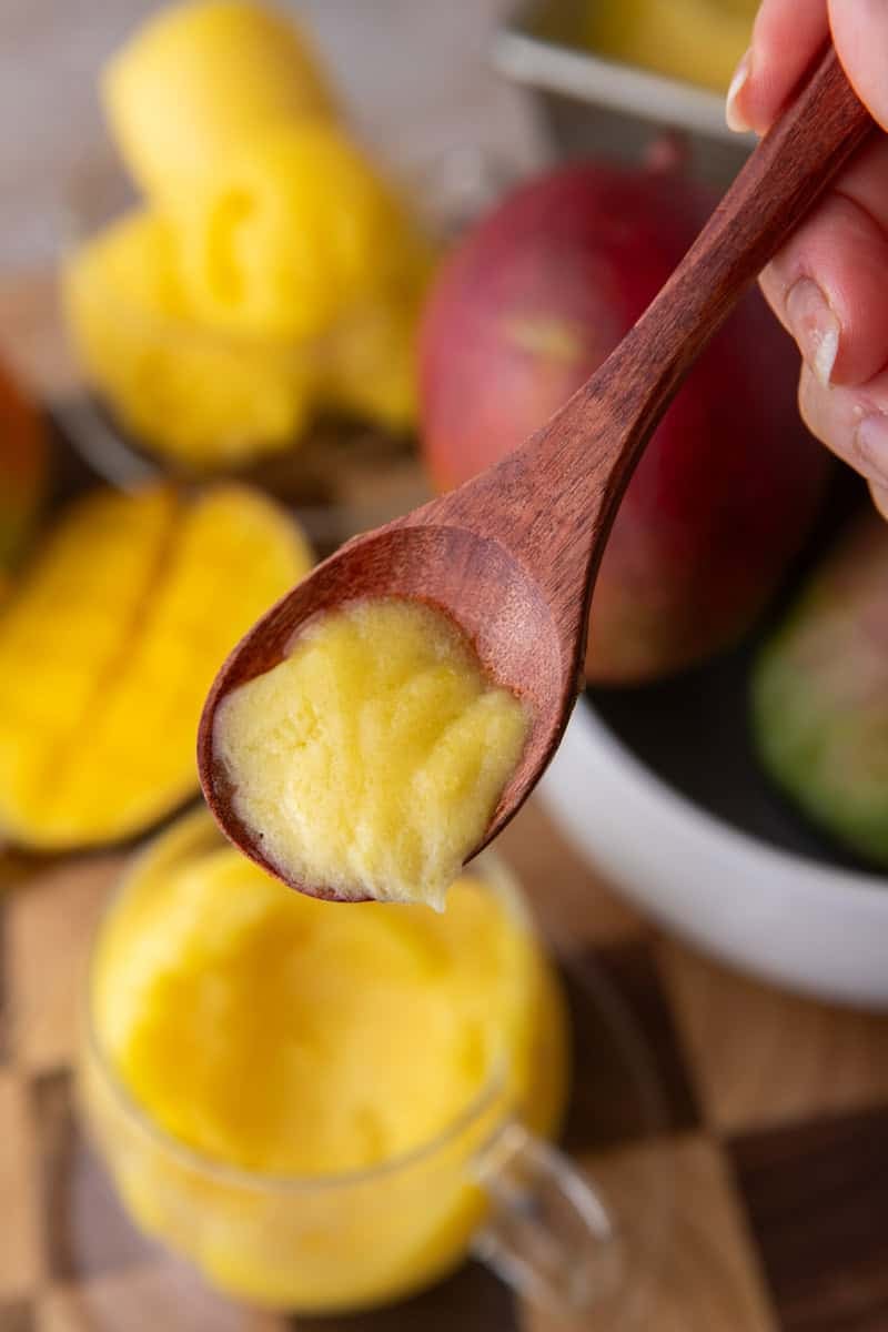 A wooden spoon holding a creamy bite of mango sorbet