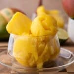 Homemade mango sorbet scoops in a glass dish with fresh mango