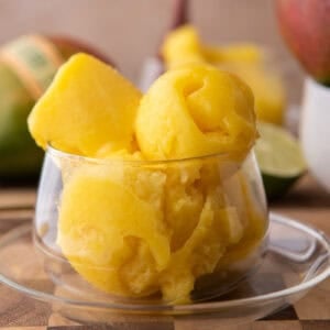 Homemade mango sorbet scoops in a glass dish with fresh mango