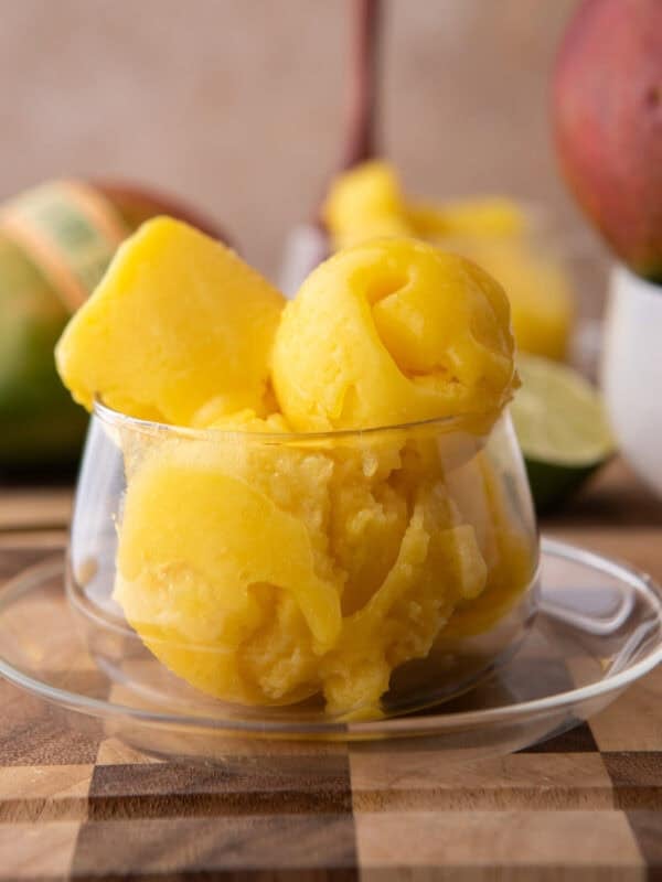 Homemade mango sorbet scoops in a glass dish with fresh mango