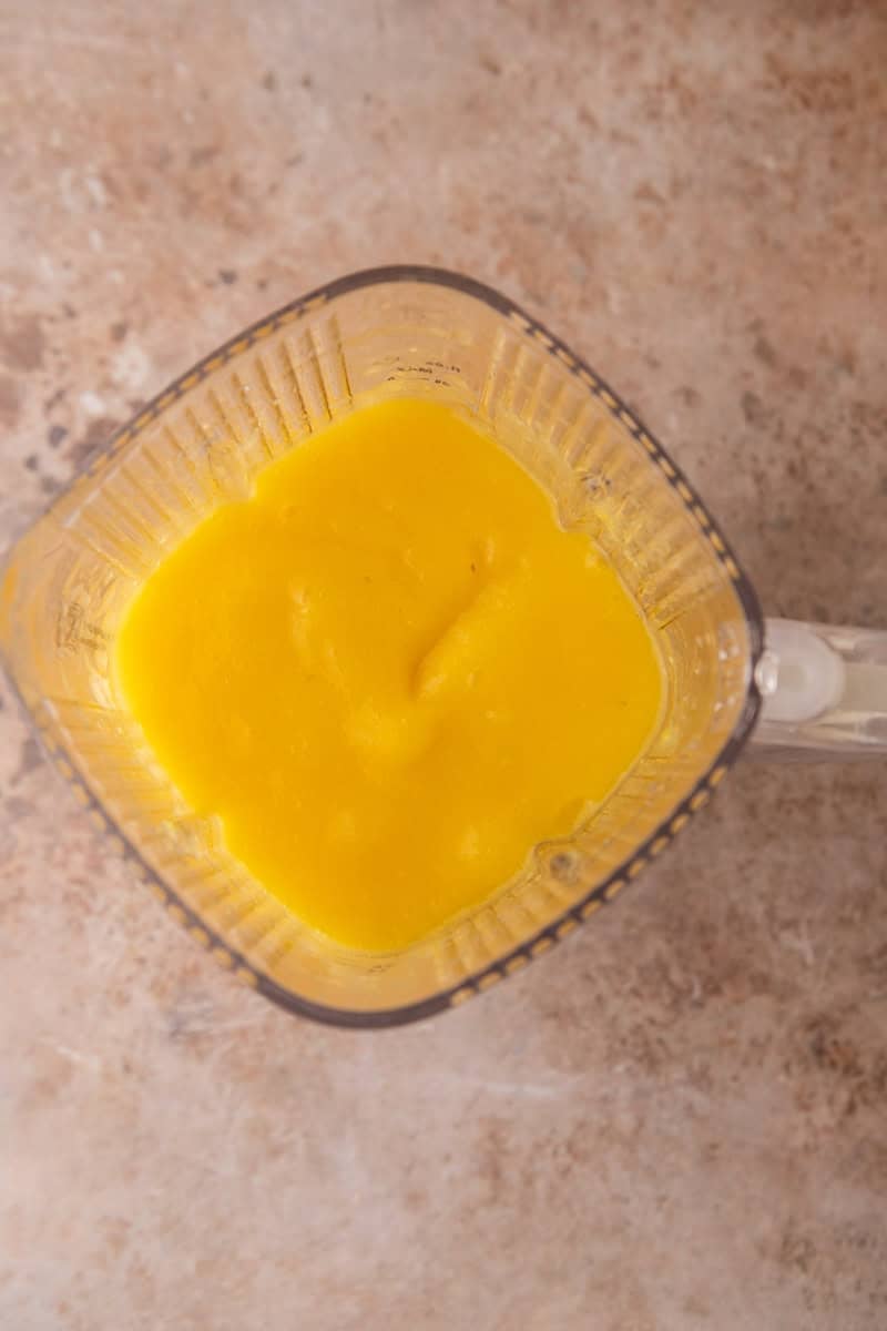 Overhead view of smooth, bright orange mango puree in a blender.