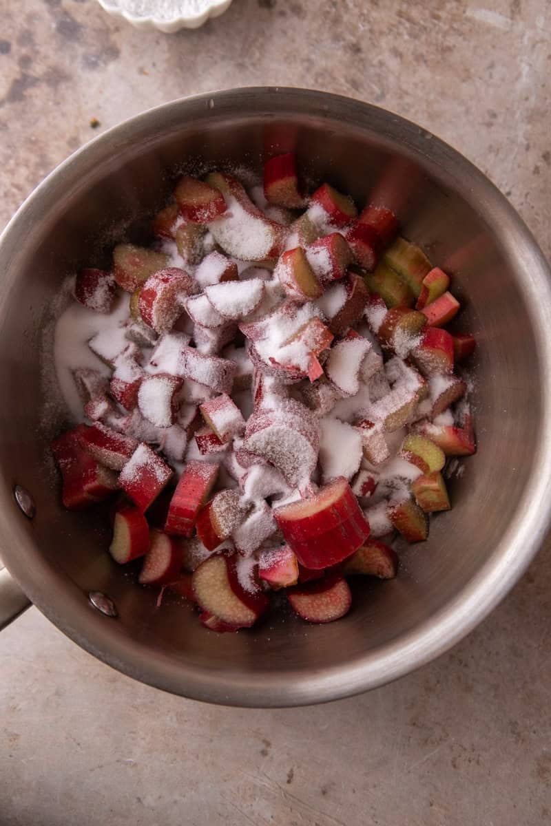 Chopped fresh rhubarb and granulated sugar combined in a stainless steel saucepan before cooking
