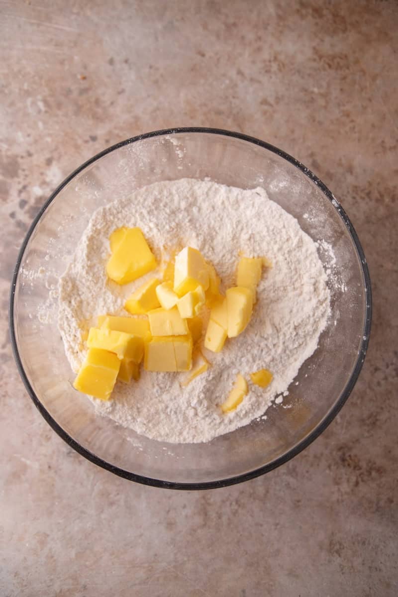 Cold cubed butter added to flour and sugar mixture in a large glass bowl to make shortbread dough