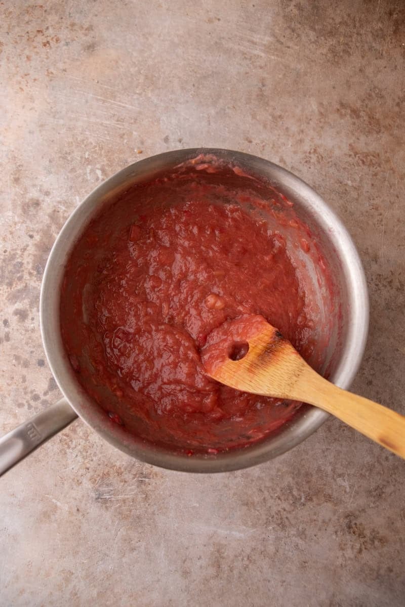 Thick jammy rhubarb filling cooked down in a saucepan with a wooden spoon, deep pink and glossy