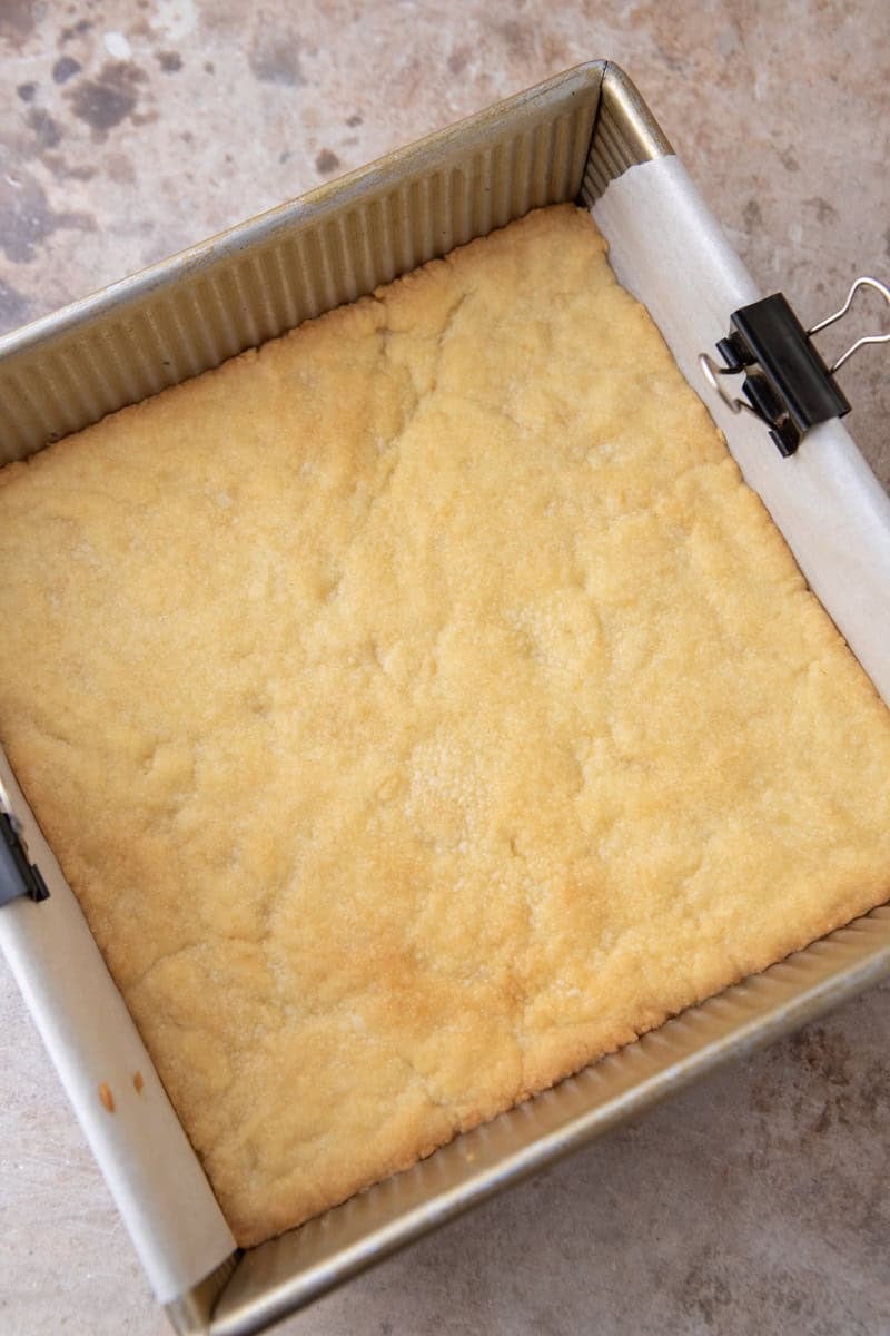 Par-baked shortbread crust in an 8x8 gold baking pan, golden and set, fresh out of the oven