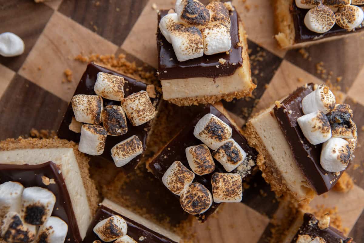 Overhead view of toasted marshmallow s'mores cheesecake bars on a wood board with chocolate ganache and charred marshmallows