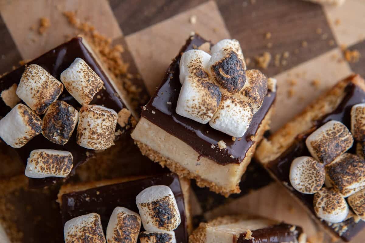 Three finished s'mores cheesecake bars from above with toasted mini marshmallows piled over chocolate ganache