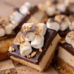 A single s'mores cheesecake bar topped with toasted mini marshmallows and crushed graham crackers on a wooden checkerboard board