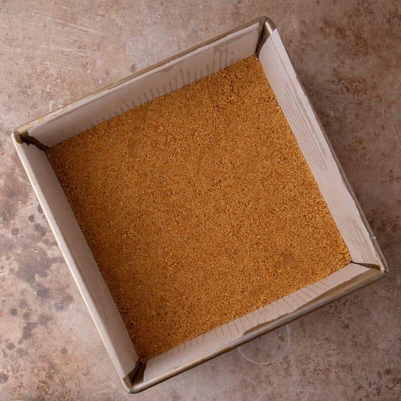 Graham cracker crust pressed evenly into a parchment-lined 8x8 pan