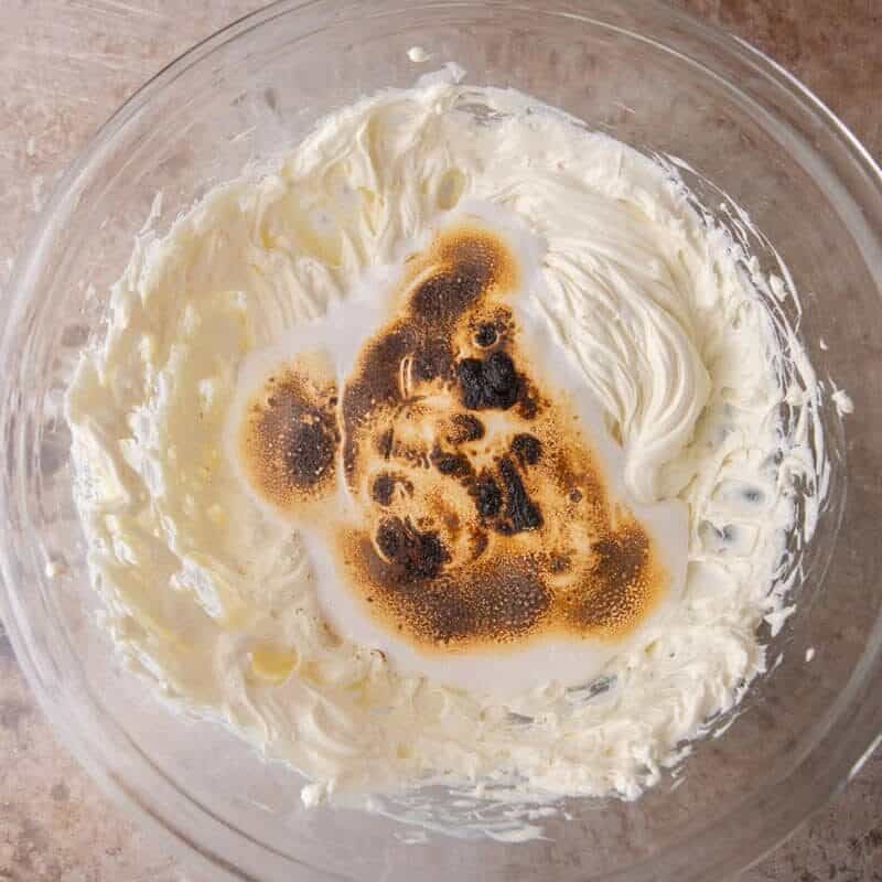 Toasted marshmallow being whipped into beaten cream cheese for the s'mores cheesecake bar filling