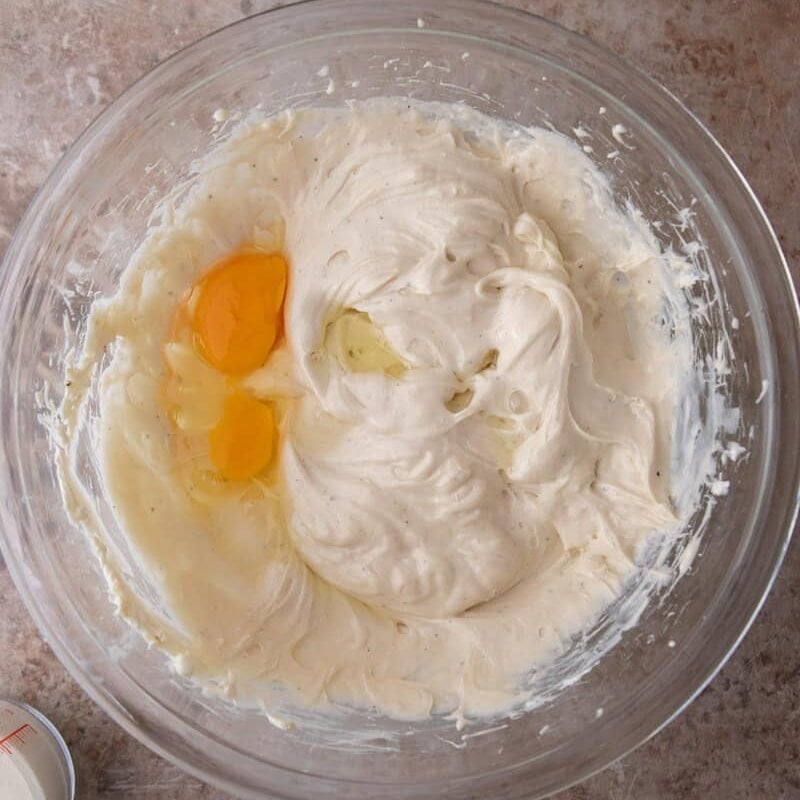 An egg being added to the marshmallow cream cheese filling for s'mores cheesecake bars