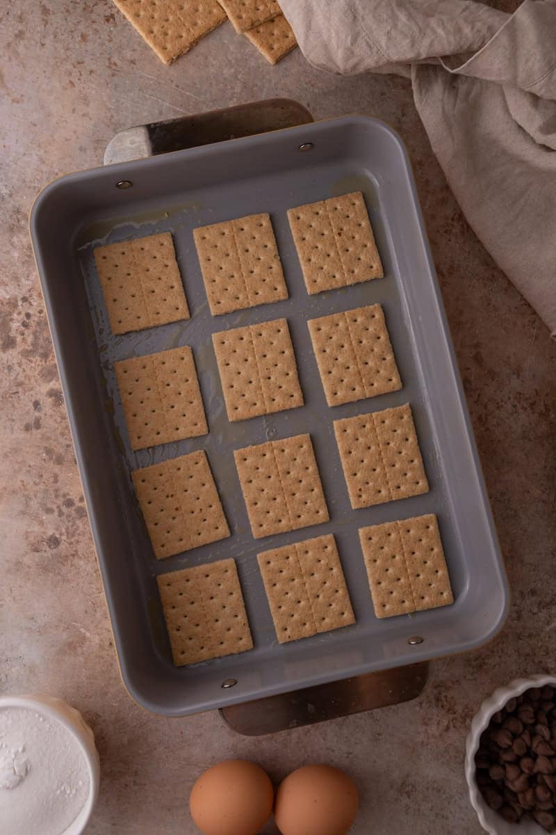 Graham cracker squares arranged in a greased baking pan as a base for s'mores cinnamon rolls