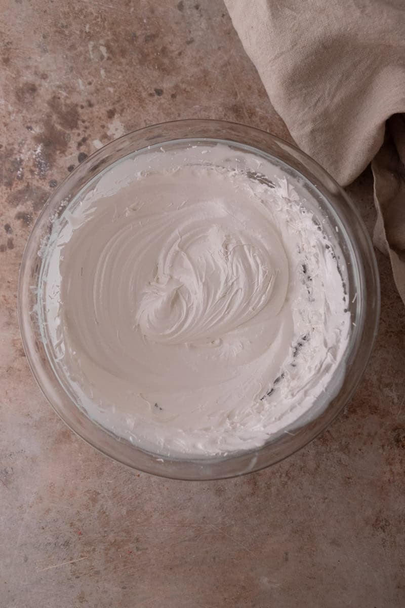 Whipped Swiss meringue with glossy stiff peaks in a glass bowl