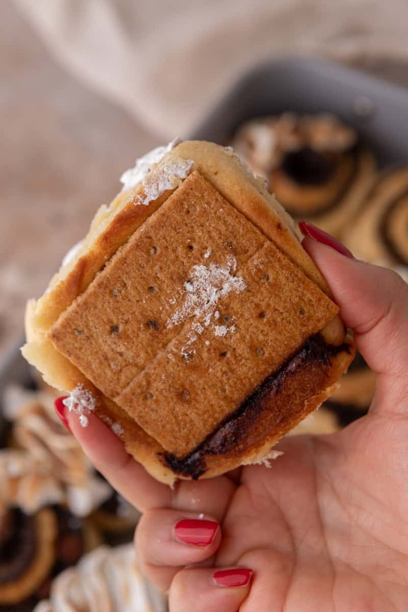 Hand holding a s'mores cinnamon roll showing the toasted graham cracker base on the bottom