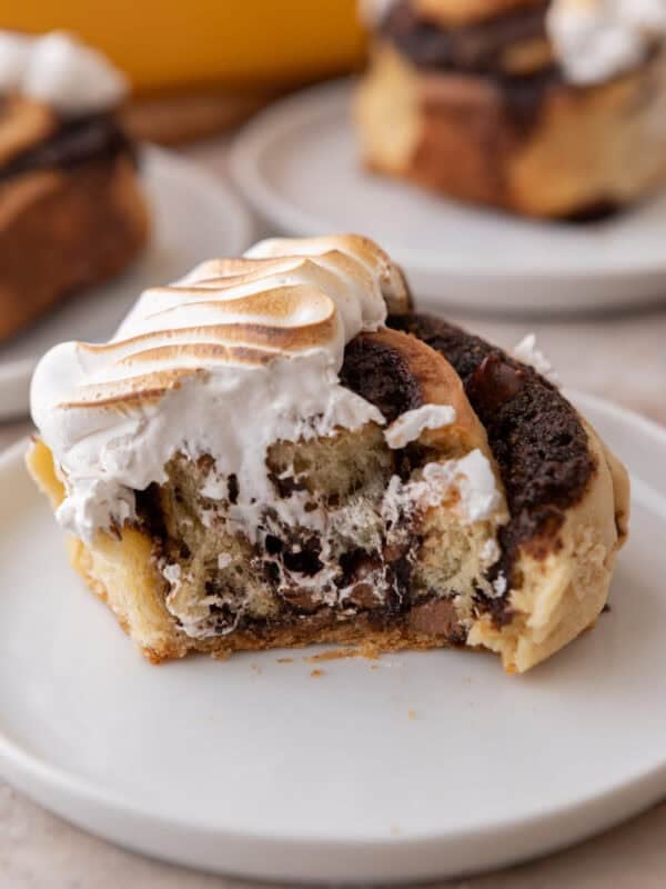 S'mores cinnamon roll topped with toasted meringue on a white plate with a bite taken out