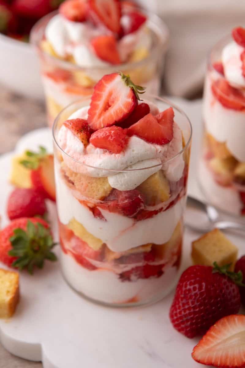 Strawberry shortcake trifle cups in clear glasses topped with whipped cream and a halved strawberry