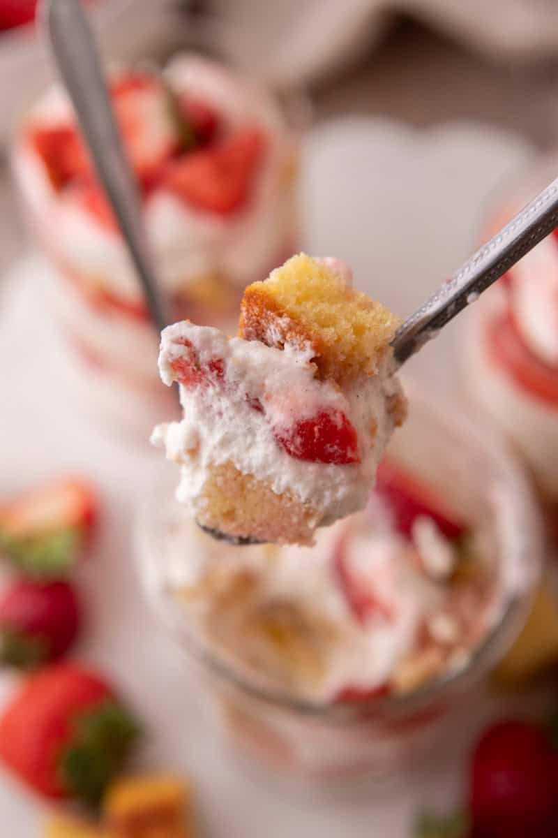 A spoonful of strawberry shortcake trifle with vanilla cake, whipped cream, and juicy strawberries lifted from the glass