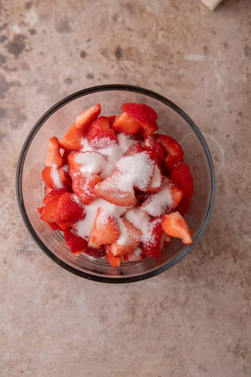 Diced fresh strawberries tossed with granulated sugar in a glass bowl