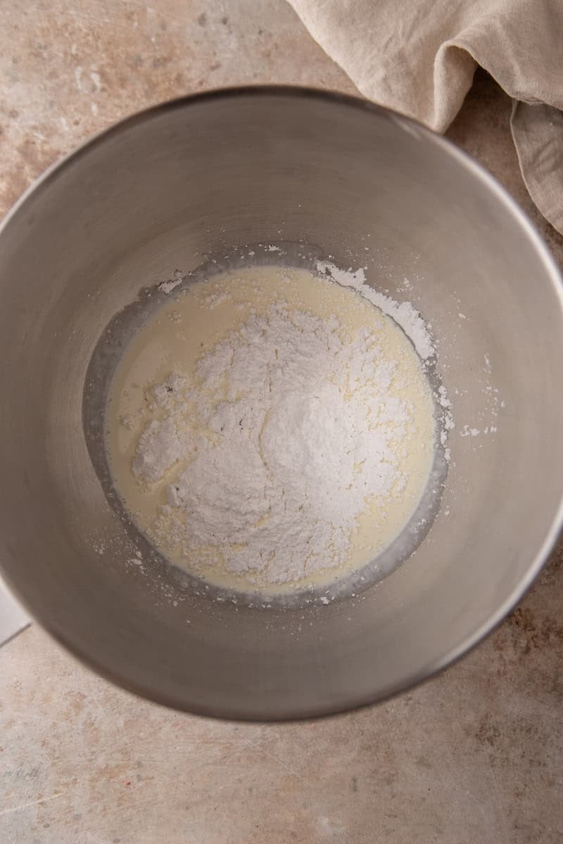 Cold heavy cream and powdered sugar in a stainless steel mixing bowl before whipping