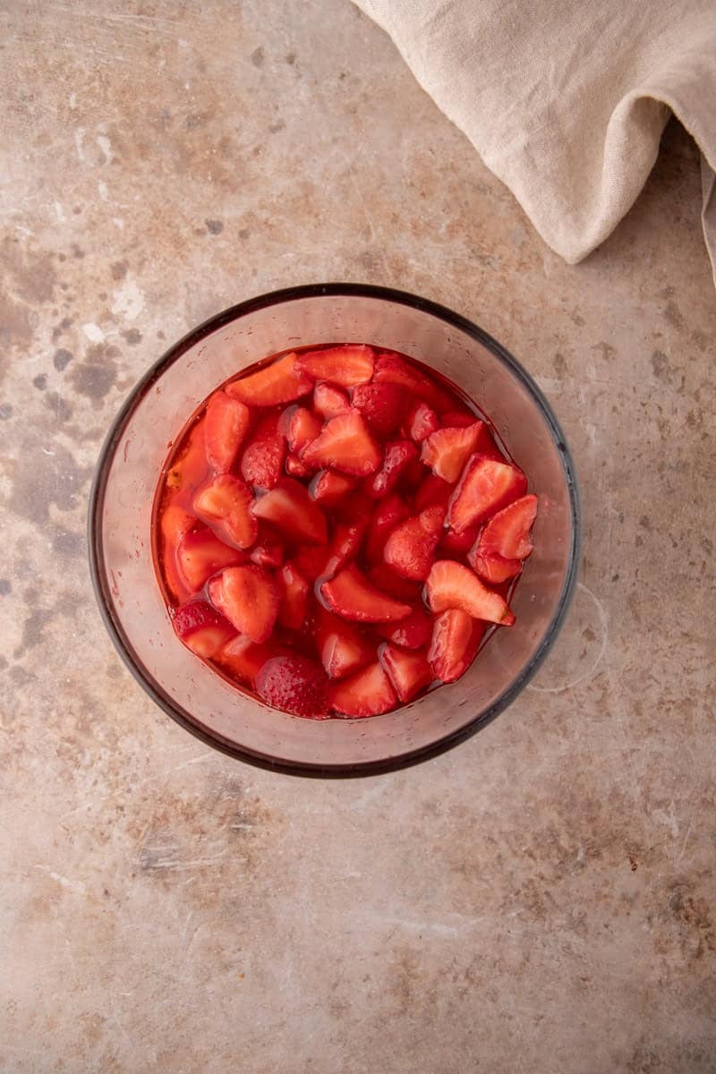 Macerated strawberries sitting in their own ruby red syrup in a glass bowl