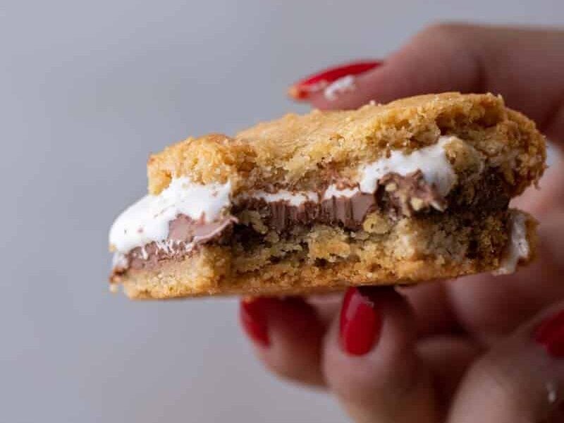 Hand holding a gooey s'mores cookie bar with melted chocolate and toasted marshmallow.