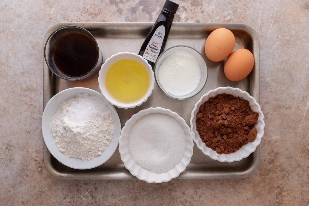 Ingredients for the chocolate sponge cake layer arranged on a sheet pan including flour, Dutch-process cocoa powder, sugar, vegetable oil, eggs, buttermilk, vanilla extract, and brewed coffee