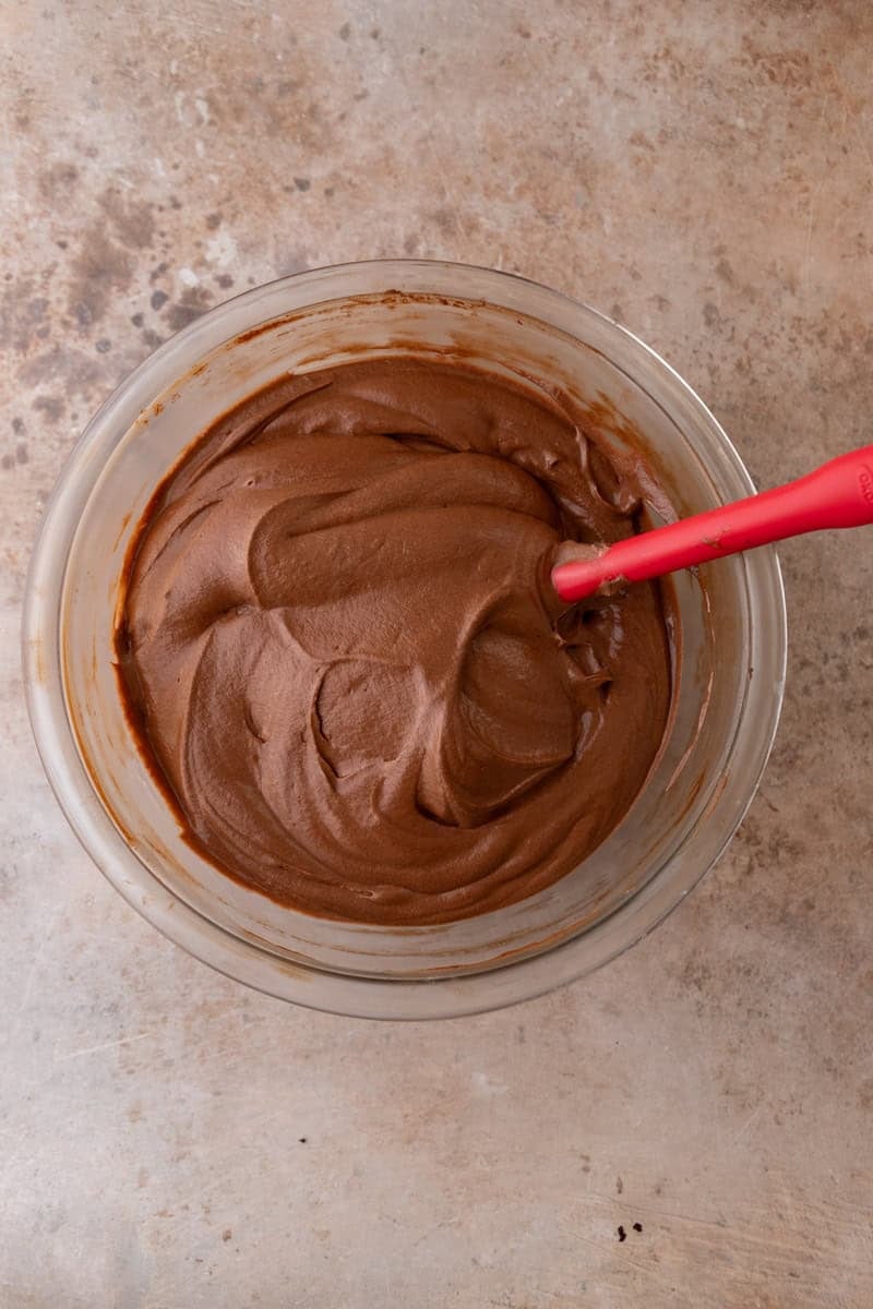 Finished chocolate mousse in a glass bowl, smooth and silky with a red rubber spatula