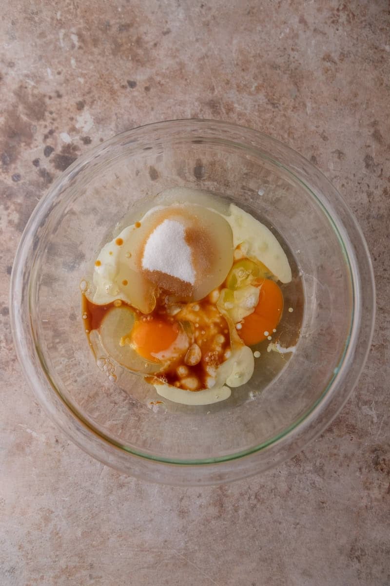 Eggs, sugar, vegetable oil, buttermilk, and vanilla extract combined in a glass mixing bowl before whisking