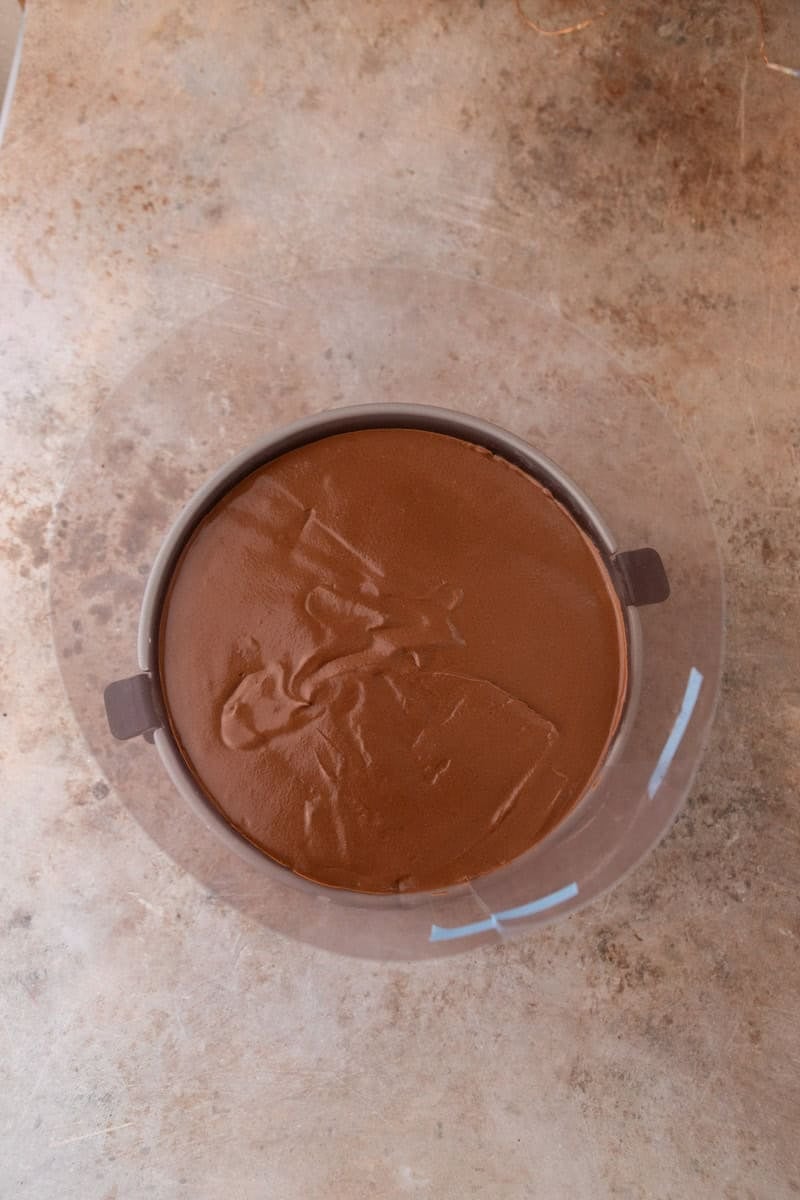 Chocolate mousse poured over the cake layer inside the springform pan with acetate collar, smoothed flat on top