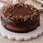 Chocolate mousse cake with glossy ganache and chocolate curls on a white scalloped marble cake stand.