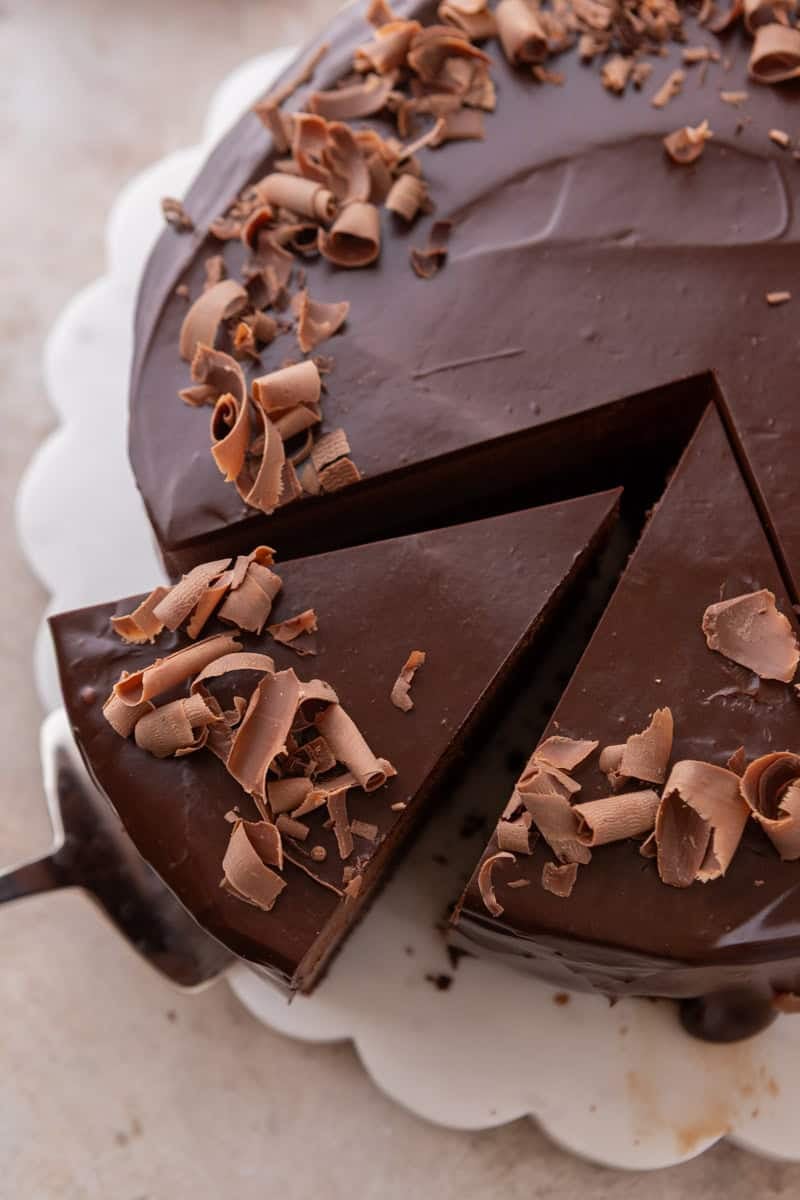 Overhead view of mousse cake topped with chocolate curls, with one slice being lifted out by a cake server