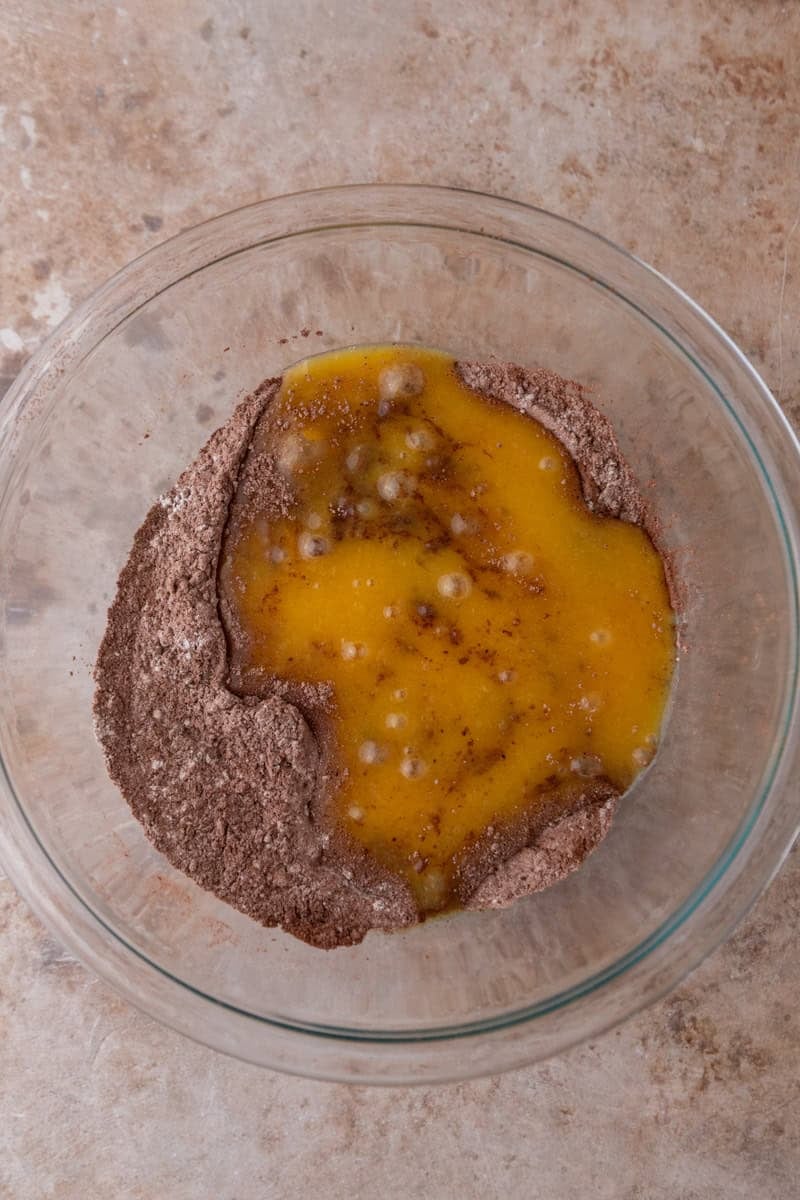 Wet ingredients poured over the dry cocoa powder and flour mixture in a glass mixing bowl