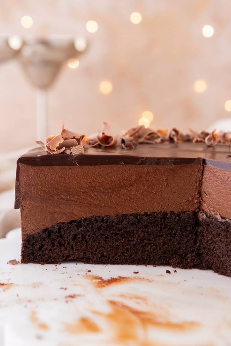 Close-up cross-section of chocolate mousse cake showing the dark chocolate sponge base, thick airy chocolate mousse middle layer, and glossy chocolate ganache top with chocolate curls