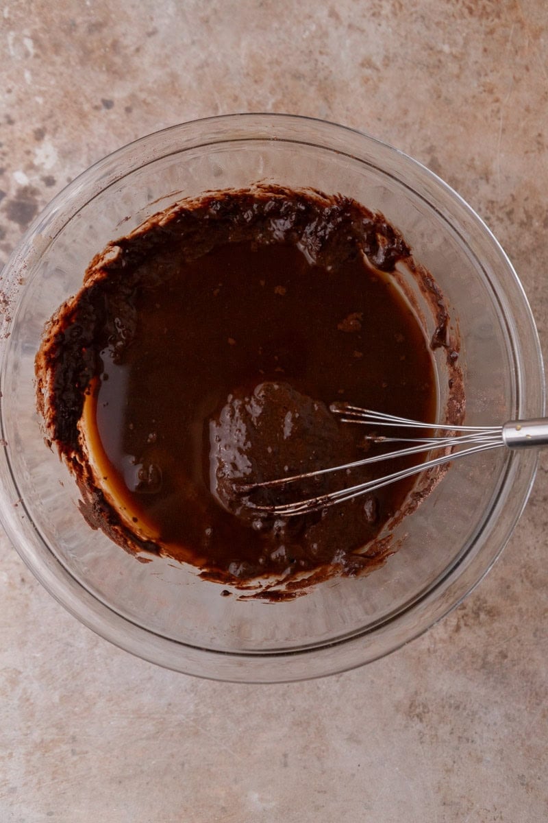 Thin dark cake batter in a glass mixing bowl with a whisk, ready to pour into the pan