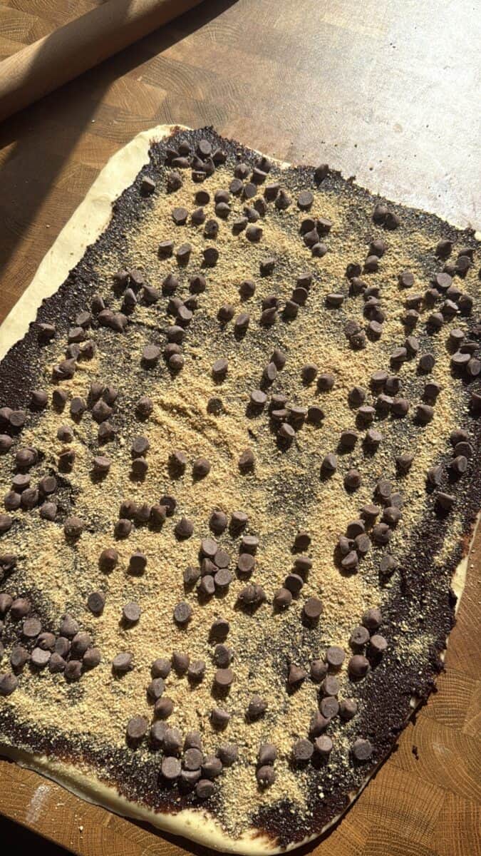 Rolled out brioche dough spread with chocolate filling, graham crumbs, and chocolate chips
