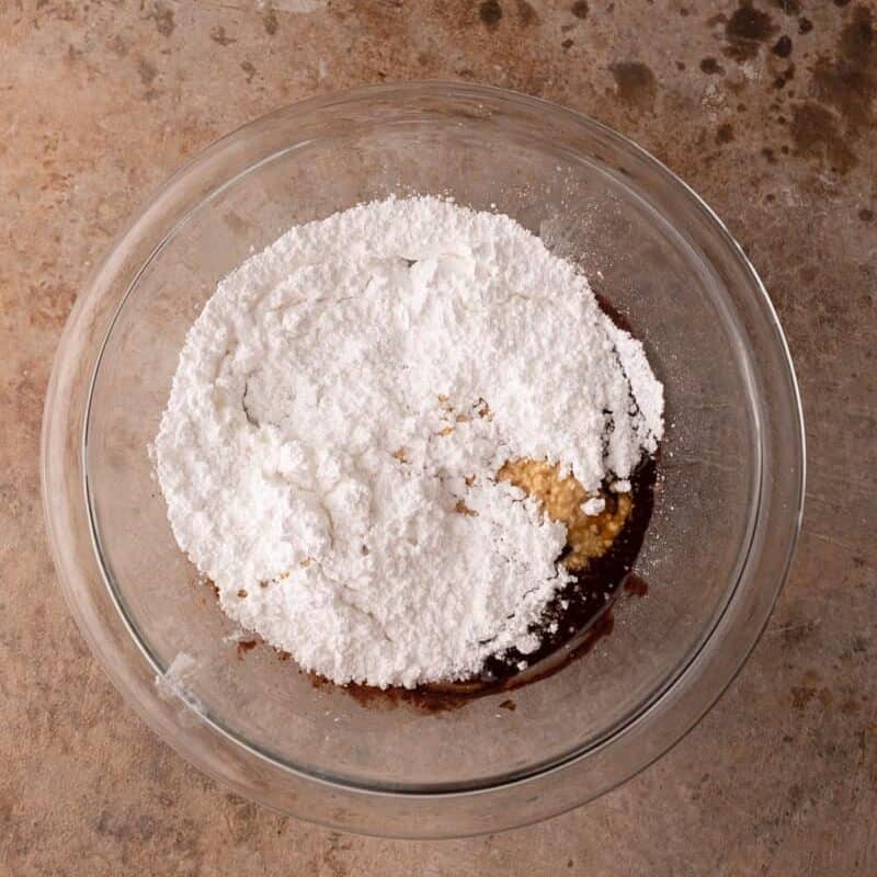 the powdered sugar of the brownie frosting recipe being added to the bowl over the butter mixture