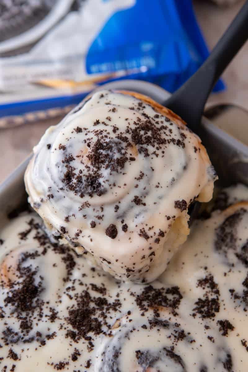 Glazed Oreo cinnamon roll topped with crushed Oreos being lifted from the pan